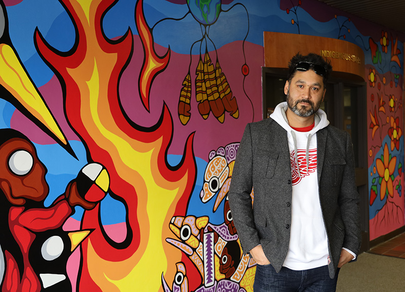 Mike Cywink stands in front of Indigenous Studies mural.